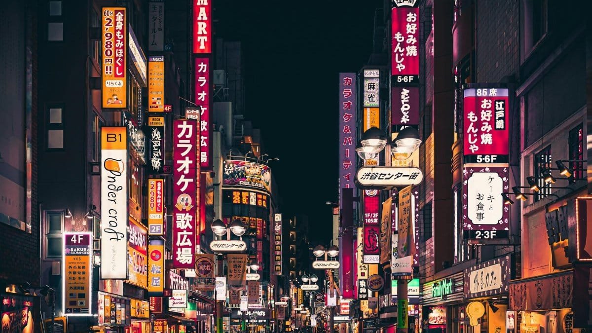 Night view of a busy Tokyo street with vibrant neon signs and people walking in Shinjuku, Japan.
