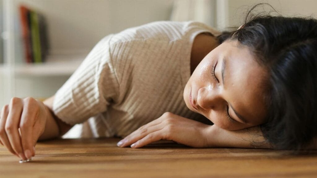 Woman lying on wooden table, appearing emotional, with a small object in hand.
