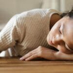 Woman lying on wooden table, appearing emotional, with a small object in hand.