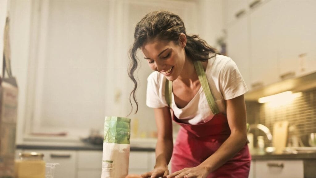 Smiling woman making dough at home, enjoying the baking process.