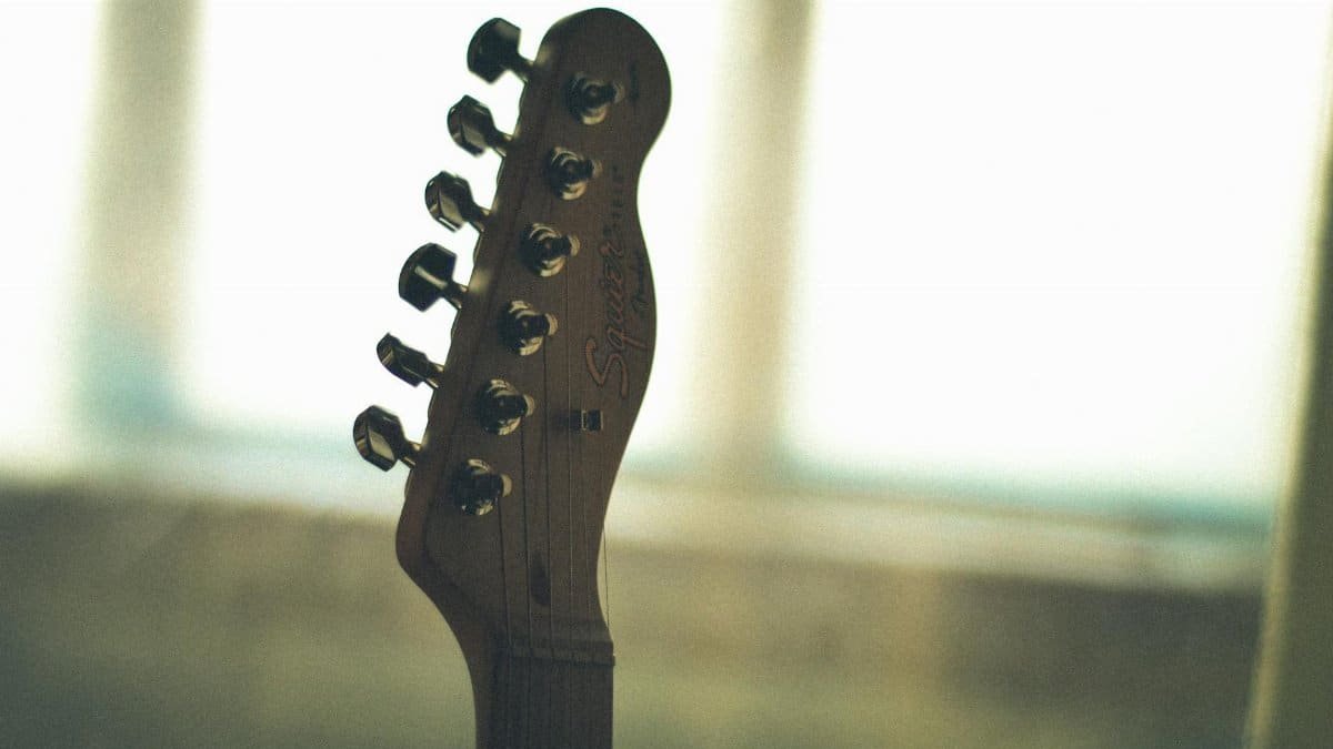 Detailed image of an electric guitar headstock with blurred background, showcasing tuning pegs and smooth wood finish.