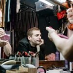 Two drag performers apply makeup backstage, showcasing identity and transformation.