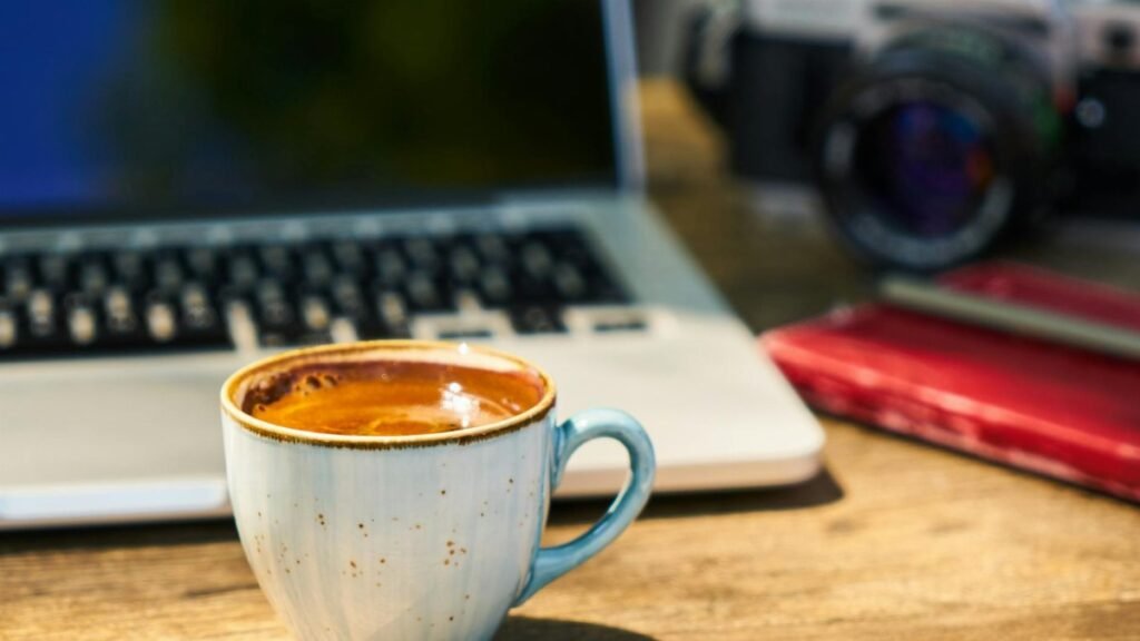 A cozy workspace with a cappuccino, laptop, and vintage camera on a wooden desk.