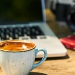 A cozy workspace with a cappuccino, laptop, and vintage camera on a wooden desk.