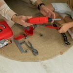 A father and son bonding over a toy tool set indoors, fostering creativity and learning.