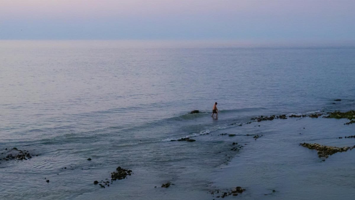 A serene twilight scene with a lone fisherman wading in the tranquil sea waters.