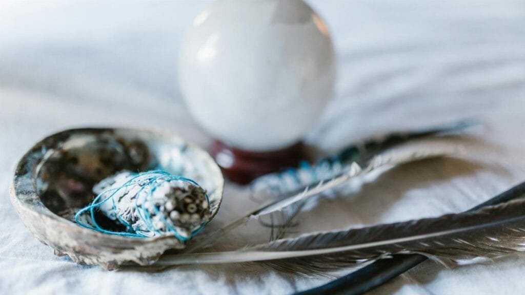 A spiritual arrangement featuring a crystal ball, sage bundle, and feathers, ideal for mystical themes.