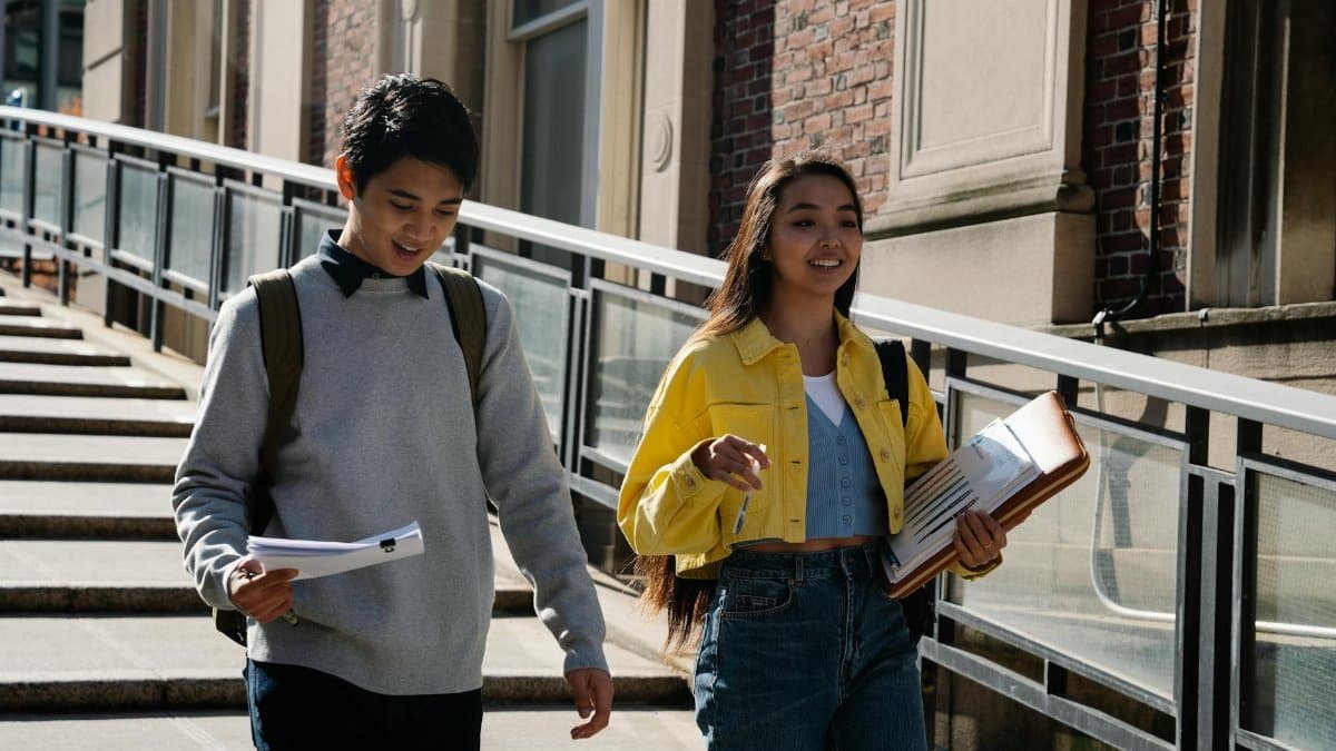Two students walking and discussing notes on campus stairs, enjoying a sunny day.