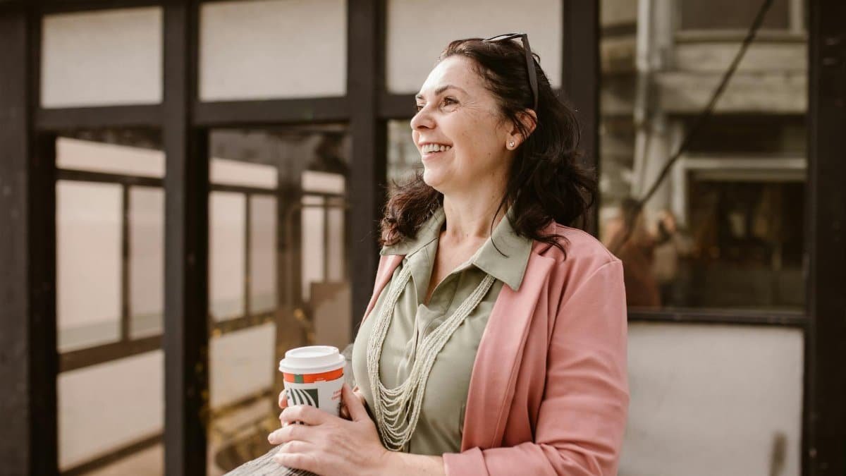 Mature woman happily holding coffee outdoors in an urban setting.