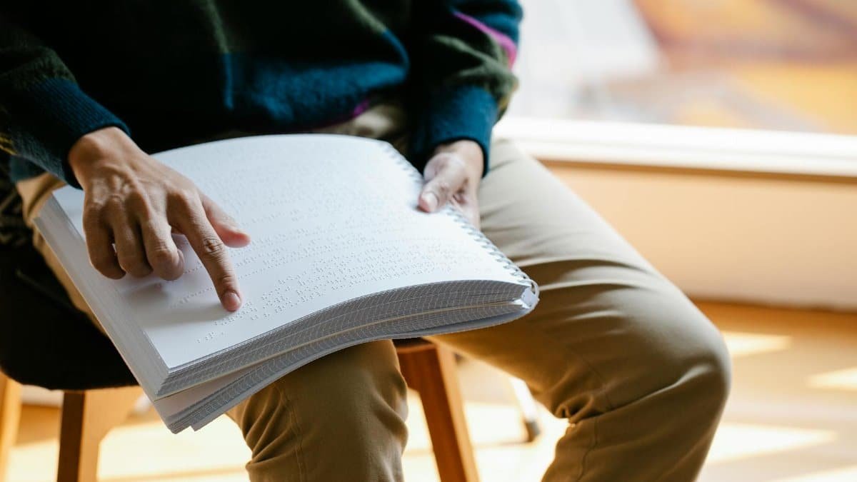 Close-up of a person reading a Braille book in natural light indoors, highlighting sensory interaction.