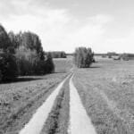 A tranquil rural path leading through a countryside landscape, captured in black and white.