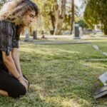 A woman kneeling by a grave in a sunlit cemetery, expressing grief and remembrance.