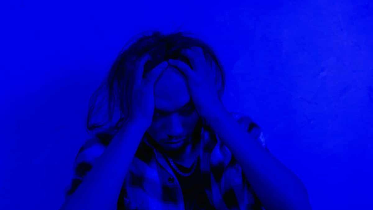 Portrait of a distressed person under dramatic blue lighting, expressing mental anguish.