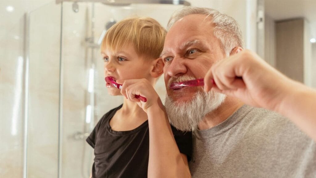 A bonding moment as a grandfather teaches his grandson about oral hygiene in the bathroom.