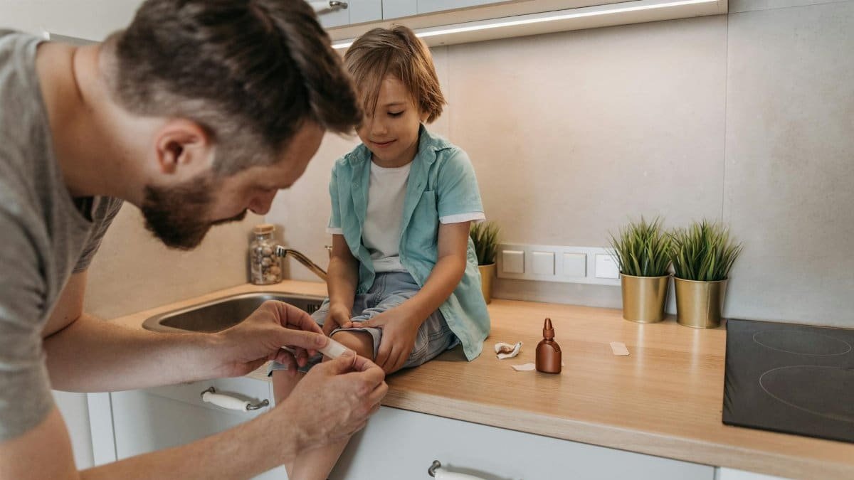 A father bandaging his child's knee on a kitchen counter, showcasing parental care.