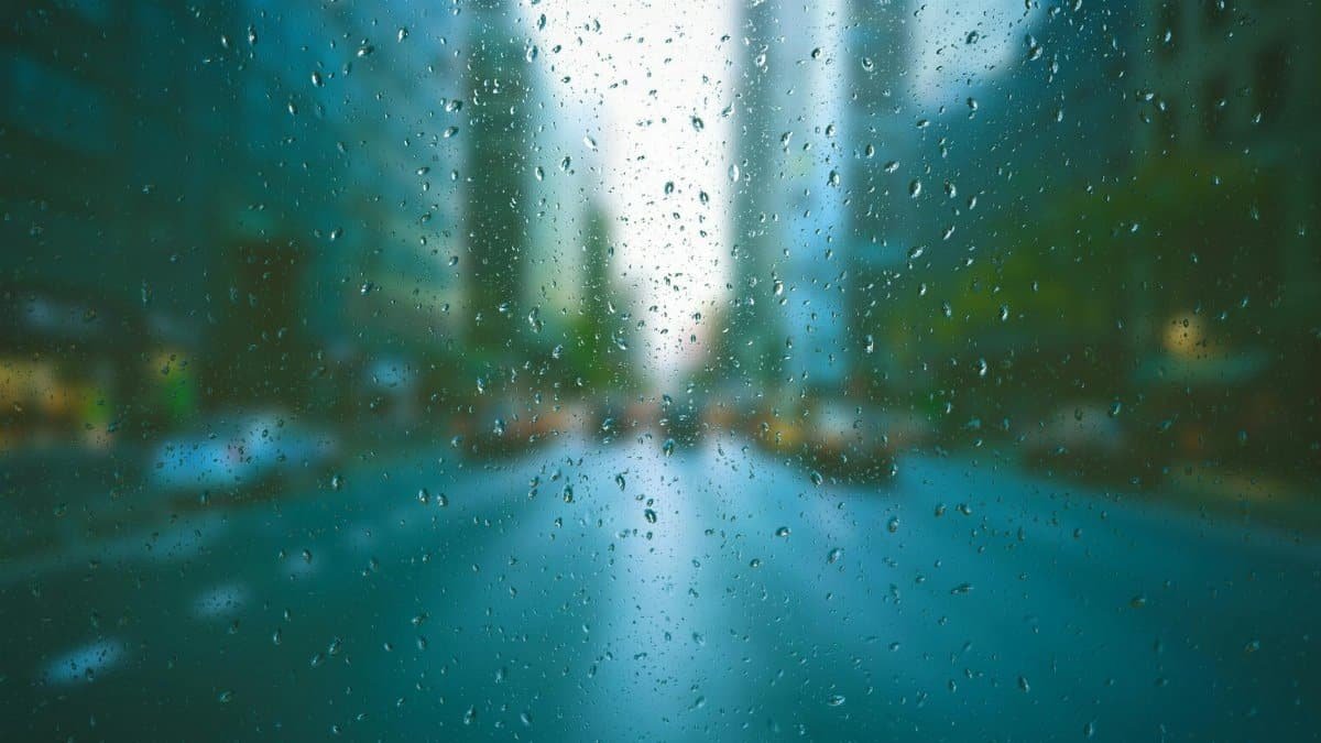 Blurred city scene through raindrop-covered window, creating a tranquil urban mood.