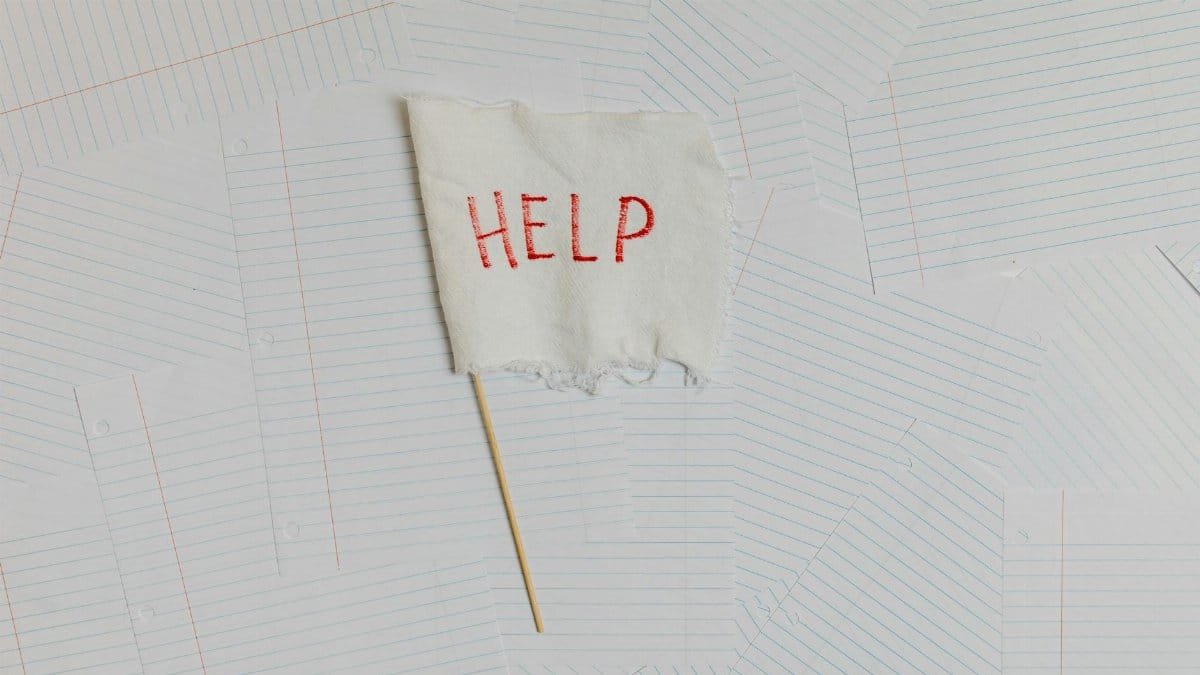 A fabric flag with 'HELP' on a scattered notepaper background, symbolizing distress or overwhelm.