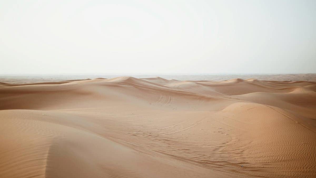 Picturesque view of endless sandy dunes in dry desert under cloudy sky in daylight