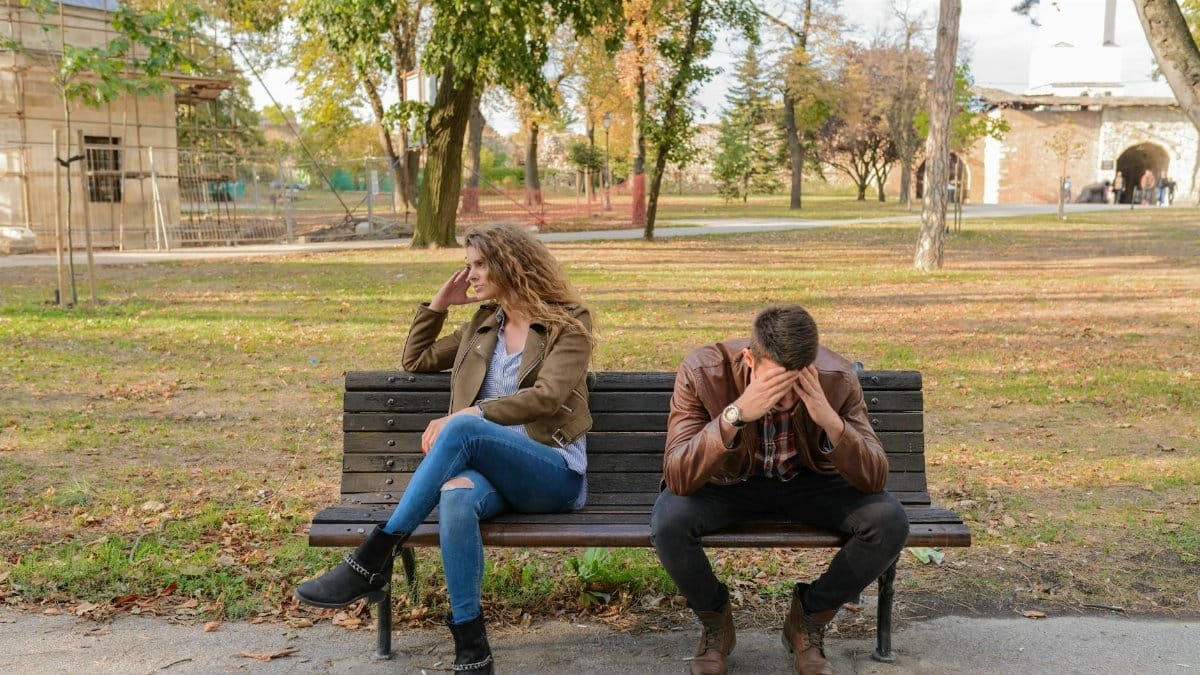 An upset couple seated on a park bench, expressing frustration during an autumn day.