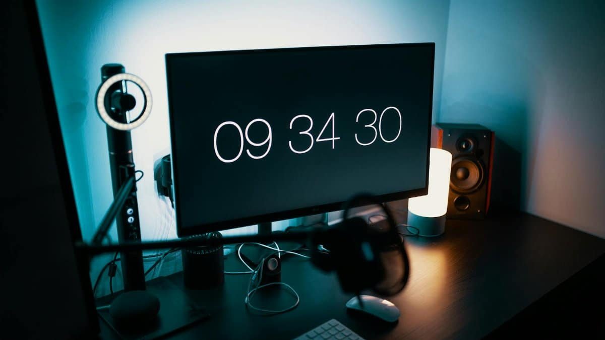 A sleek desk setup featuring a large monitor with a digital clock and ambient lighting.