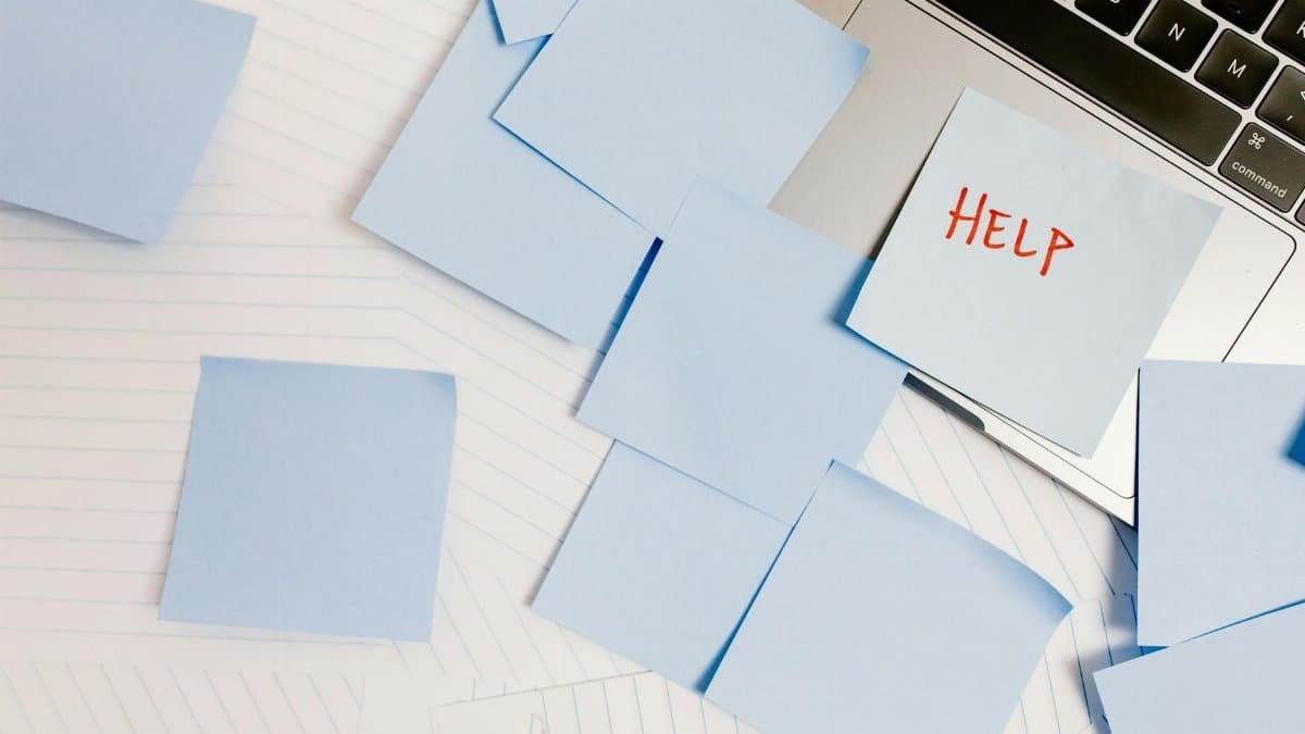 A cluttered workspace with sticky notes on a laptop, symbolizing overwhelm and need for help.