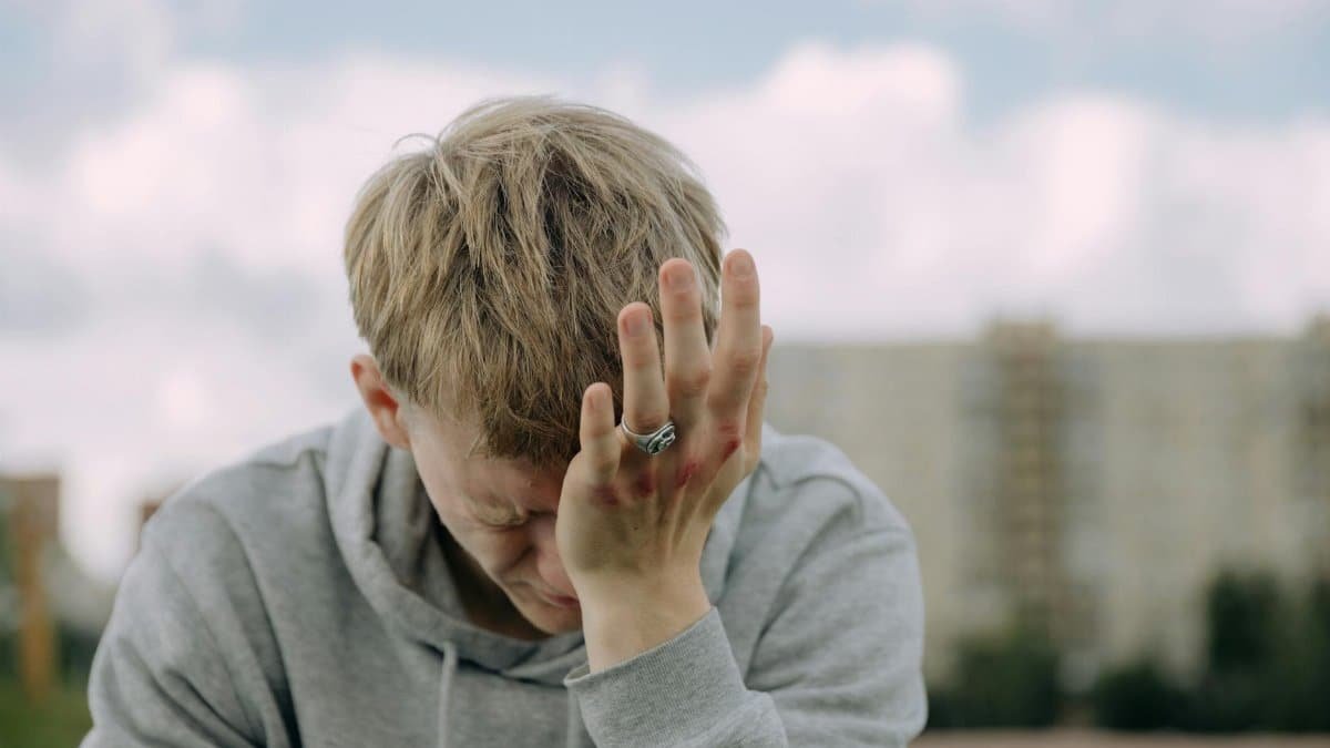 A young man outdoors holding his head in stress, depicting mental health challenges.