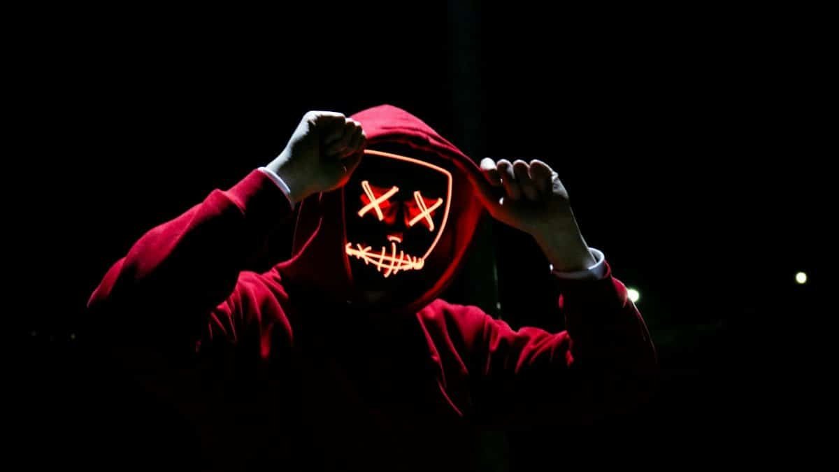 A spooky illuminated mask figure with a red hoodie in a dark setting, perfect for Halloween themes.