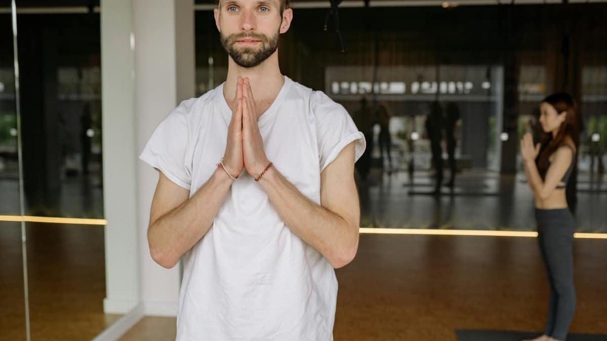 A man in a white shirt practicing yoga in a calm indoor studio, exemplifying mindfulness and relaxation.