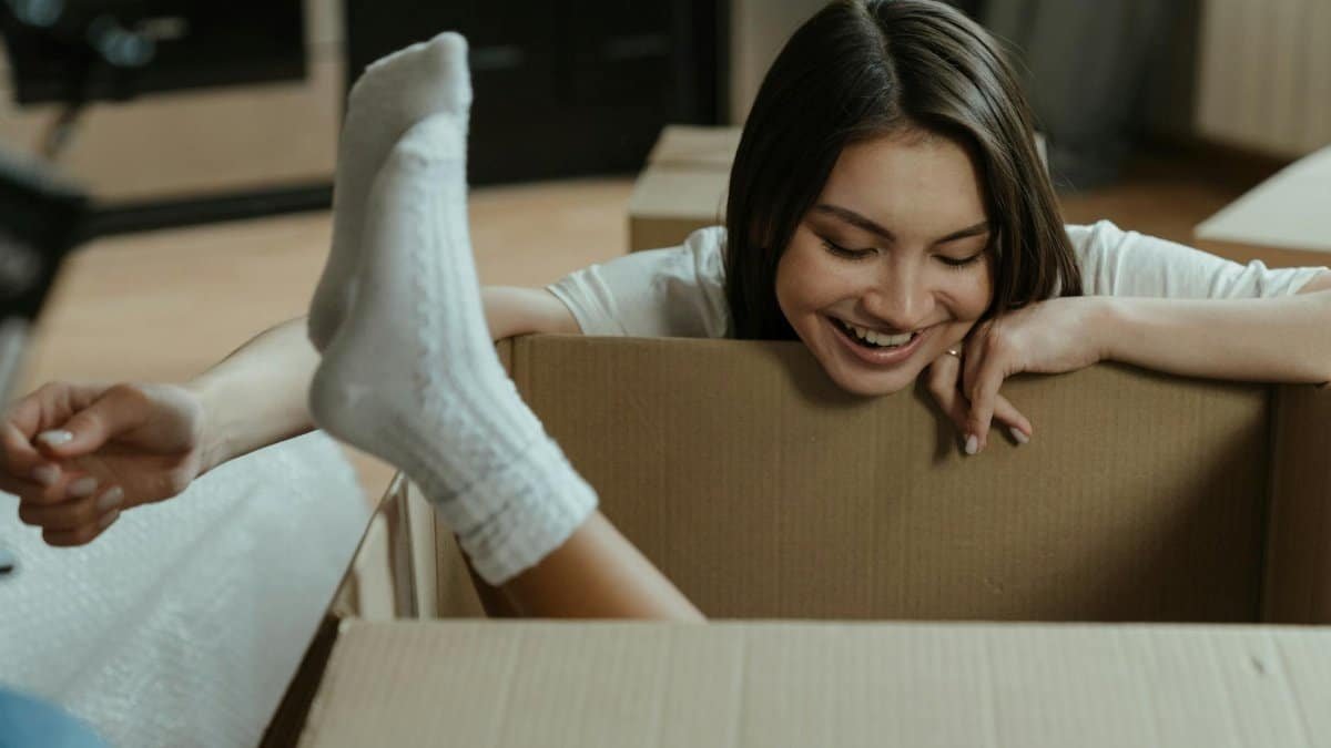 A joyful young woman plays inside a cardboard box during a fun moving day.