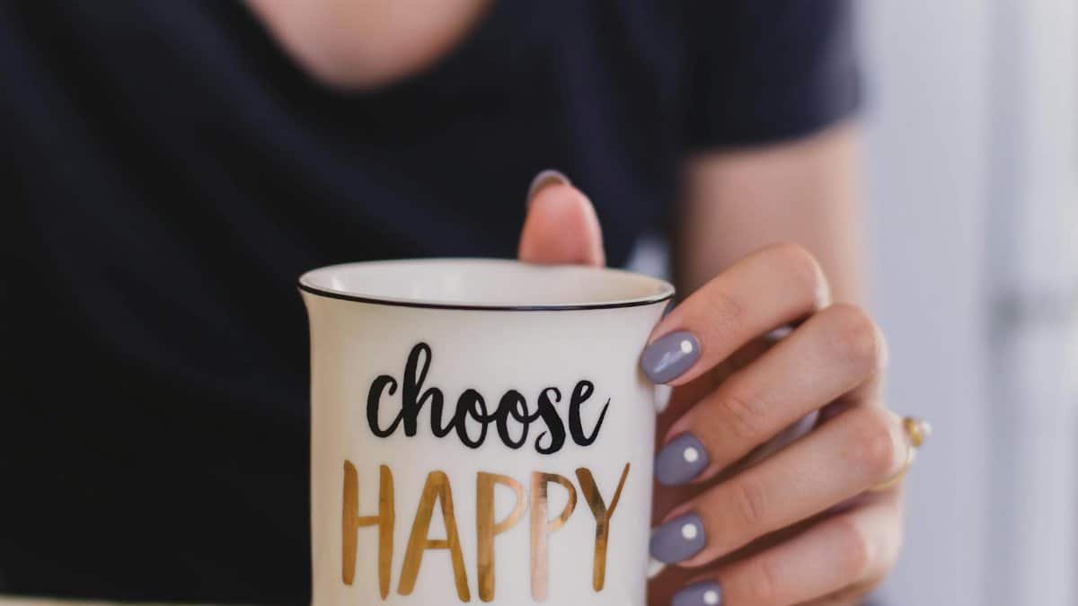 A woman holds a mug with 'choose happy' text indoors, promoting positivity.