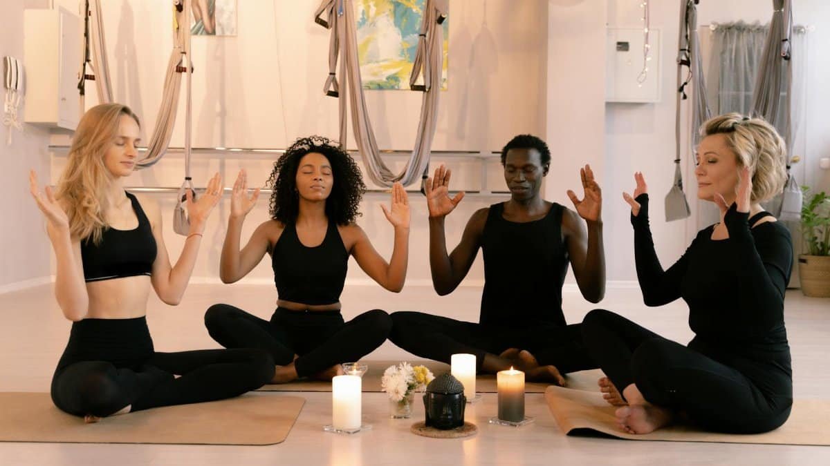 A diverse group of adults meditating in an indoor yoga studio with candles and peaceful ambiance.