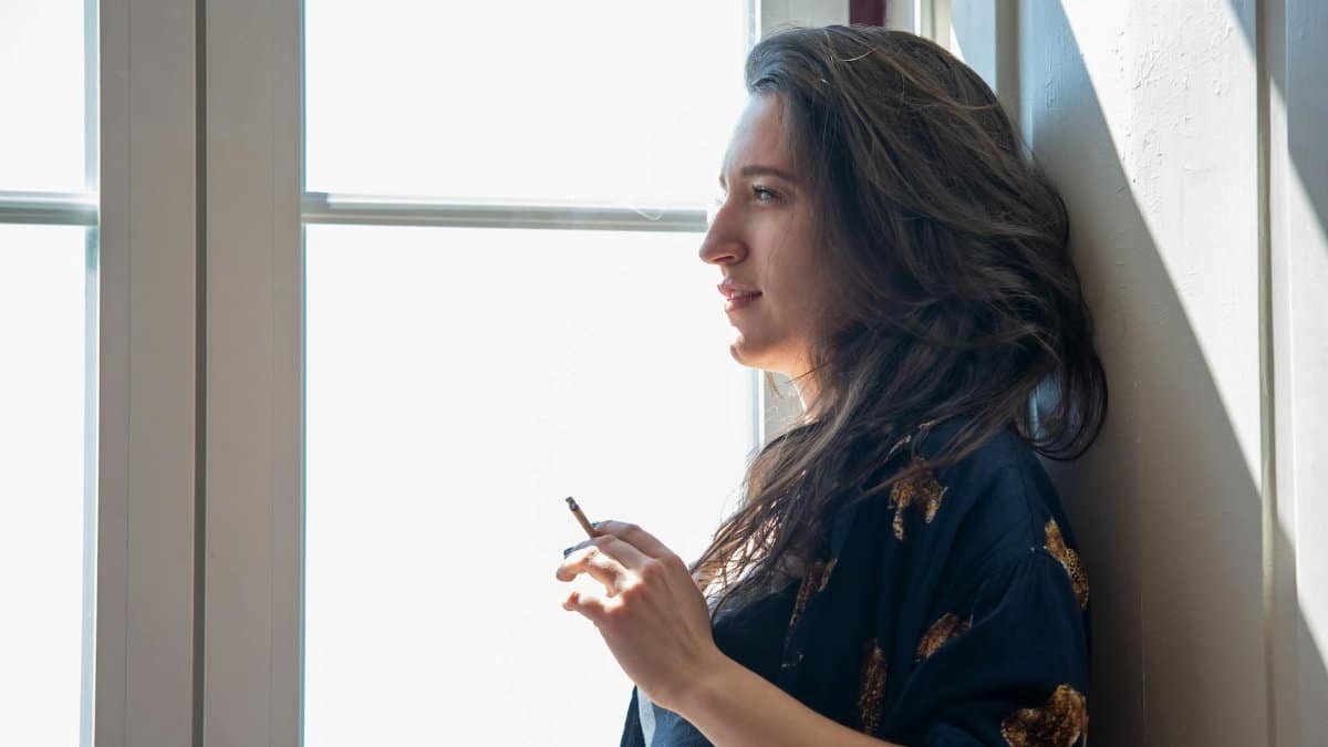 A thoughtful woman stands by a window, enjoying a moment of relaxation indoors.