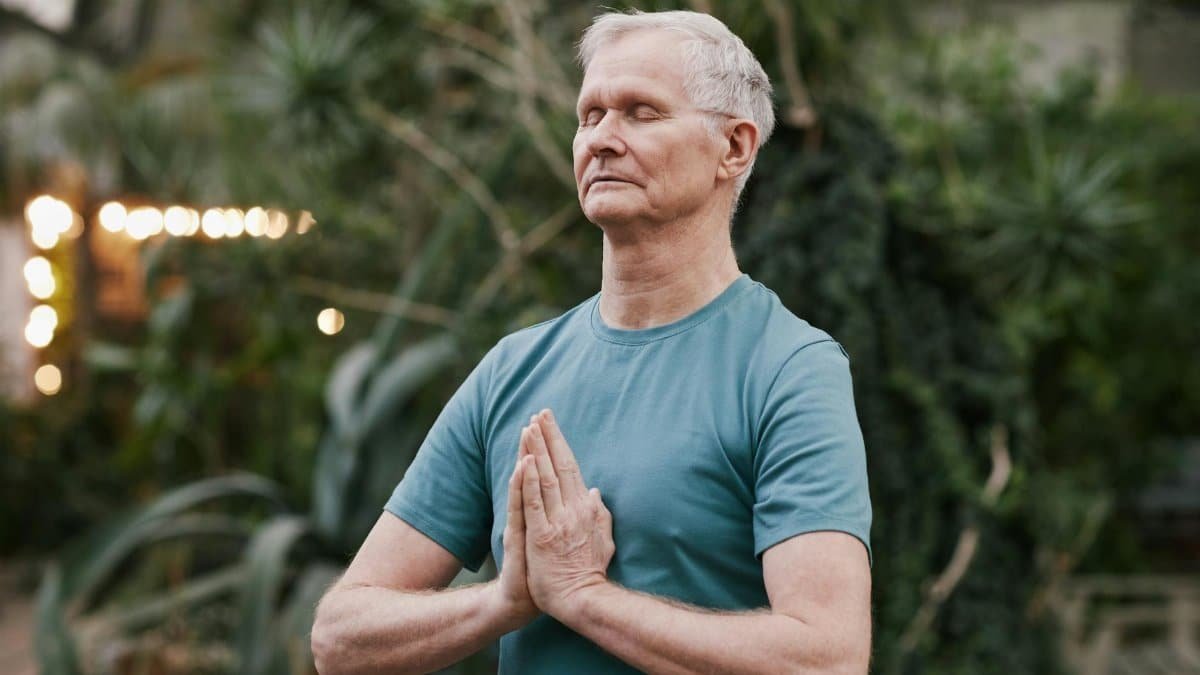 Serene elderly man meditating outdoors in a tranquil garden setting, focusing on peace and mindfulness.
