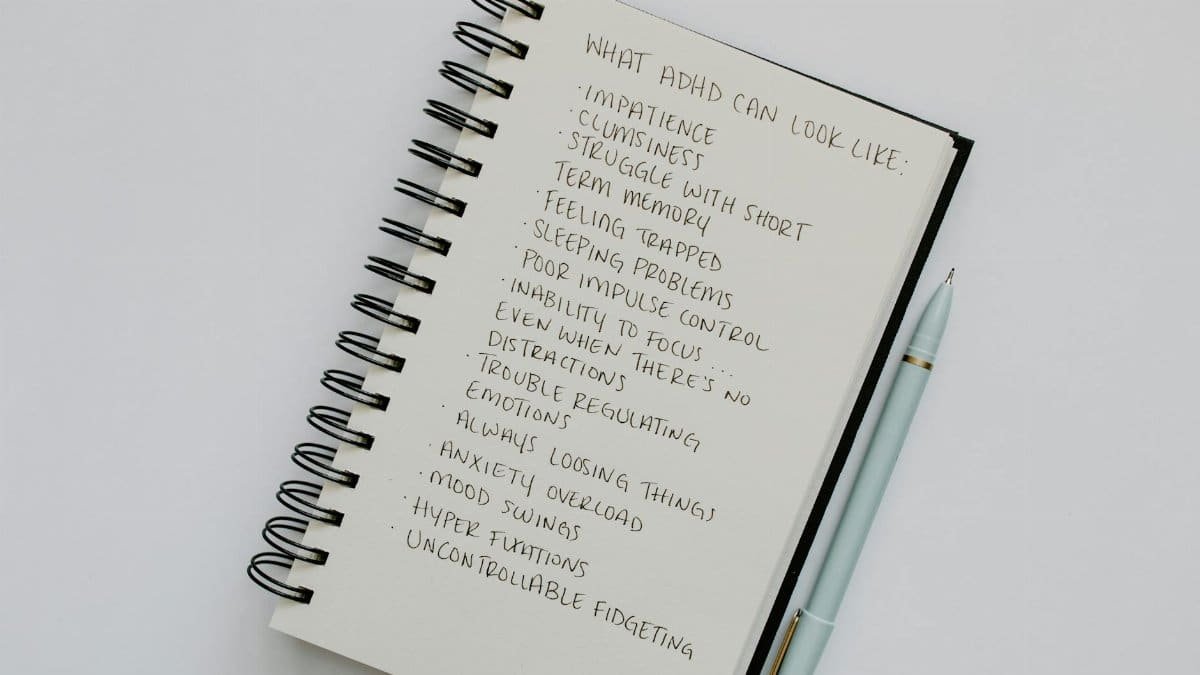 Notebook open with handwritten list of ADHD symptoms, featuring a pen alongside.