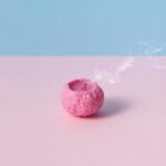 Conceptual image of a pink brain-shaped candle with smoke, on a pastel pink and blue background, symbolizing burnout.