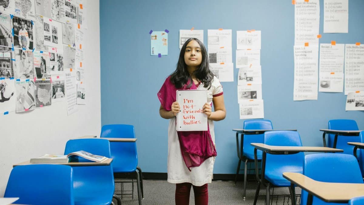 A young girl holding a sign promoting anti-bullying in an empty classroom, emphasizing awareness.