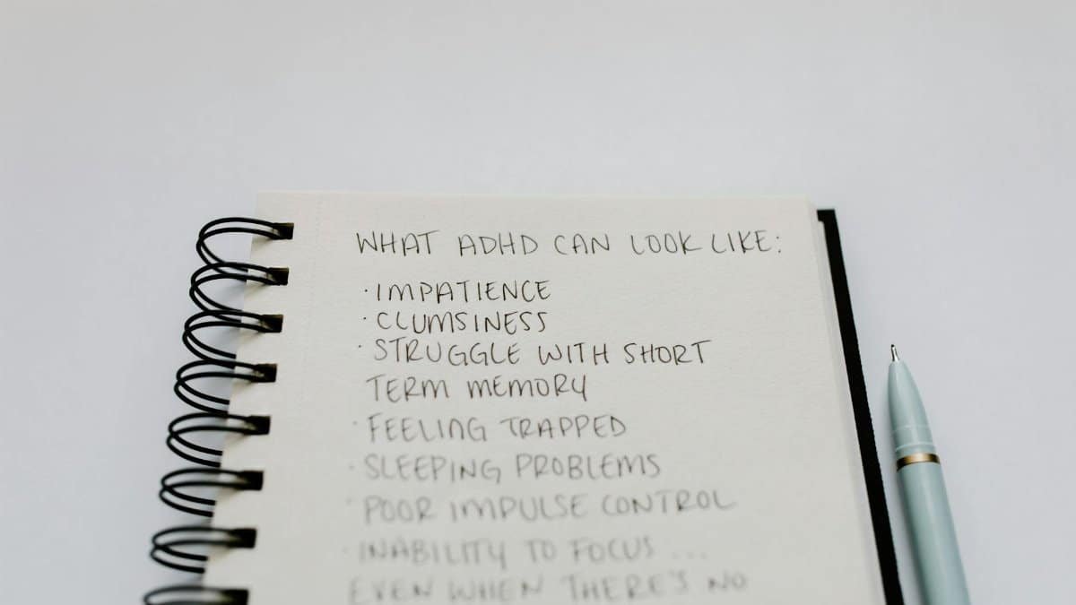 A notebook with handwritten ADHD symptoms like impatience and focus issues.