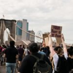 A diverse group of protesters cross Brooklyn Bridge with signs advocating for justice and solidarity.