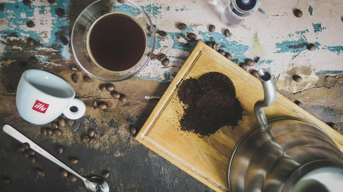 A rustic coffee arrangement featuring beans, a grinder, and a steaming cup.