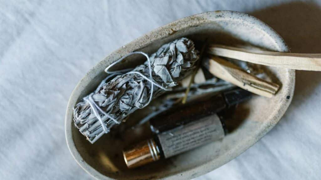 A serene still life featuring a bundle of sage, essential oils, and wooden sticks in a rustic bowl.