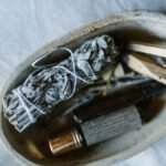 A serene still life featuring a bundle of sage, essential oils, and wooden sticks in a rustic bowl.