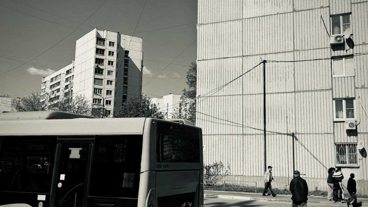 Black and white urban scene featuring a city bus and apartment buildings.