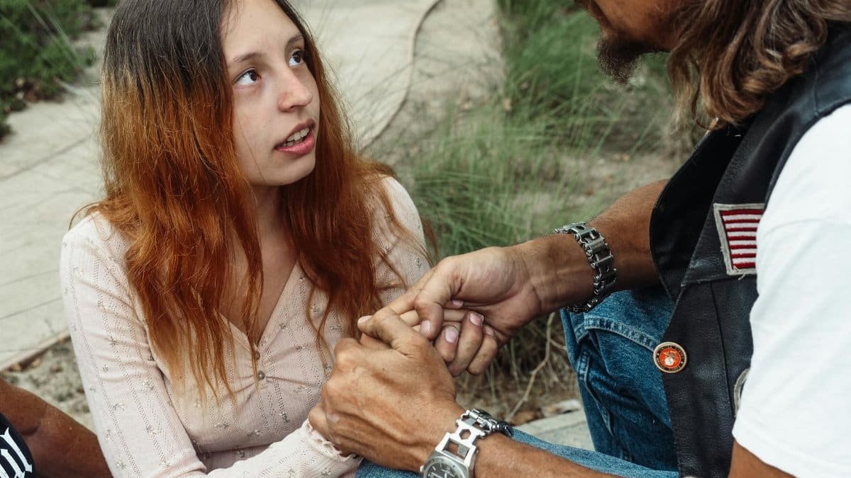 A father and daughter share a close moment outdoors, emphasizing support and bonding.