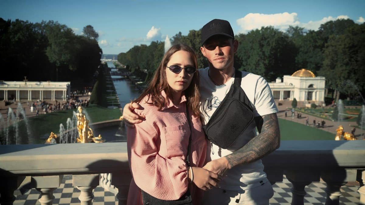 A couple poses on a sunny day with a grand palace garden and fountains in the background.