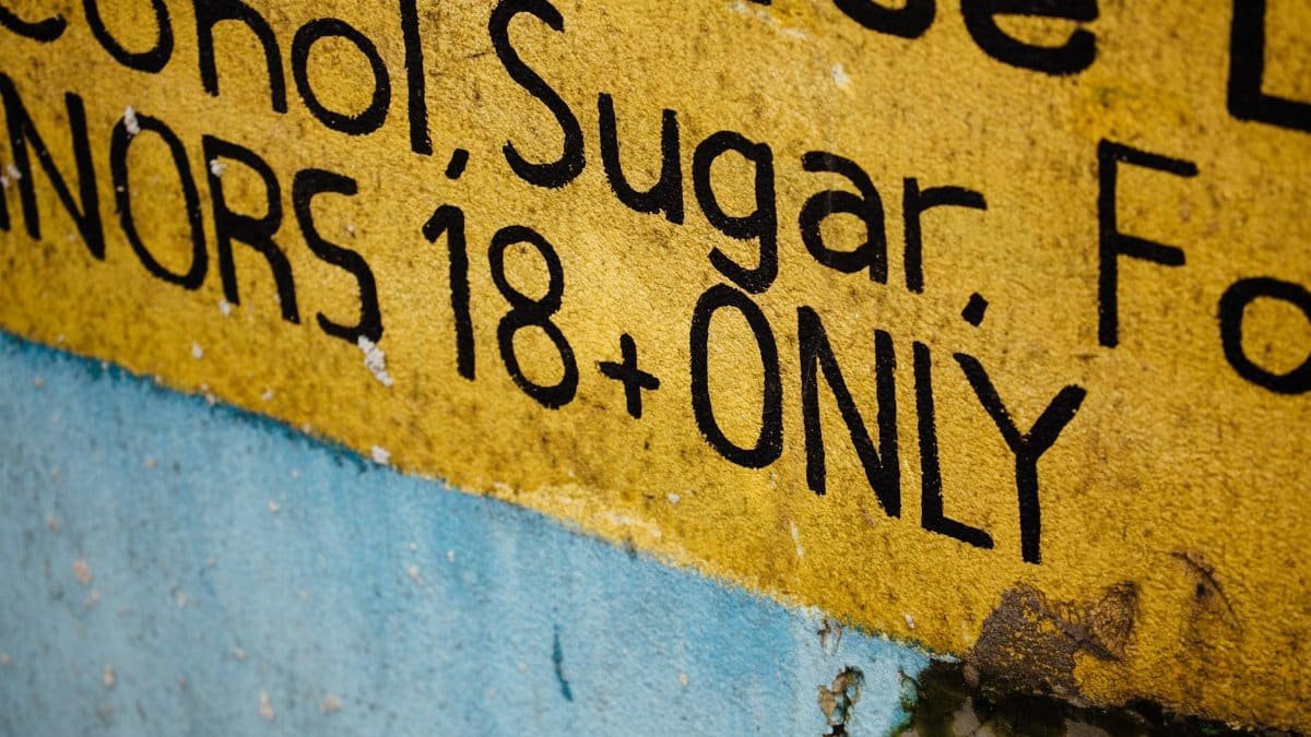 Yellow warning sign stating 'MINORS 18+ ONLY' with visible text and textured background.