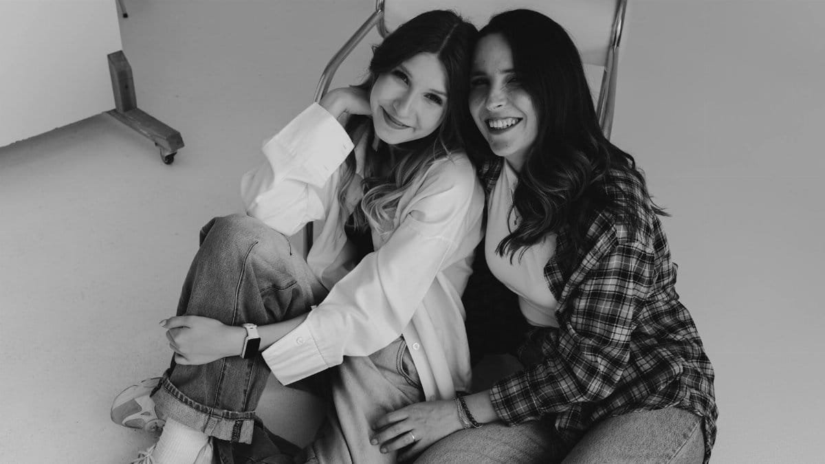 Two friends sitting together and smiling in a cozy indoor setting, captured in black and white.