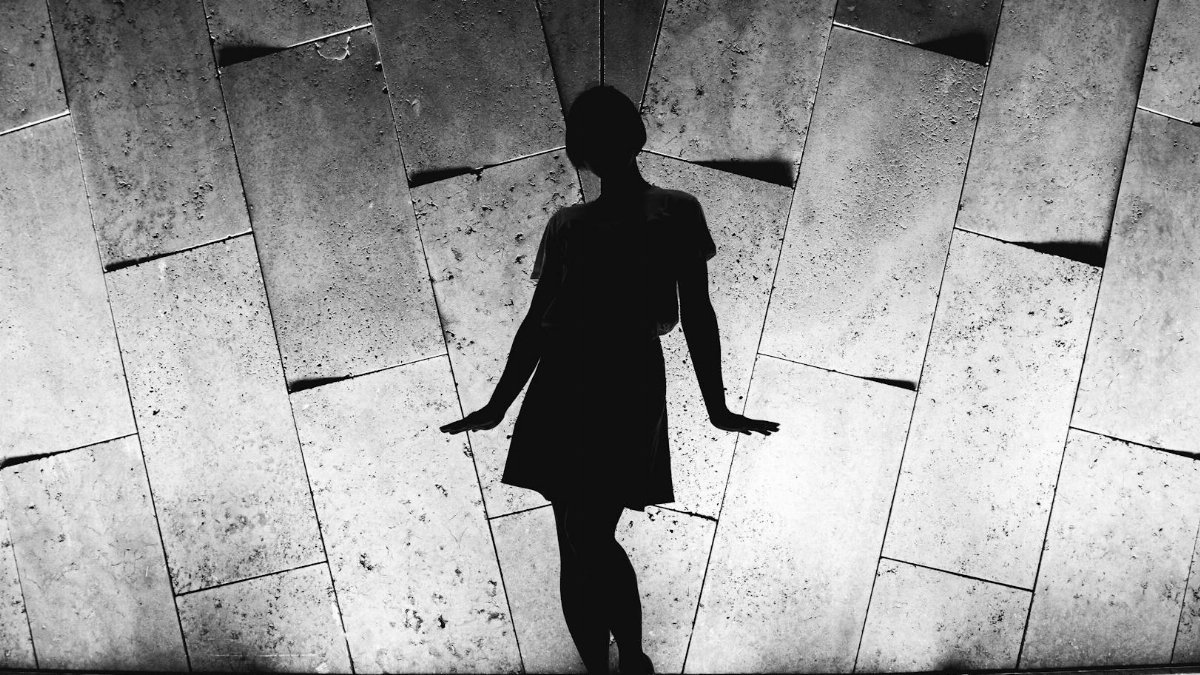 Artistic silhouette of a woman against a textured wall. Dramatic black and white photography.
