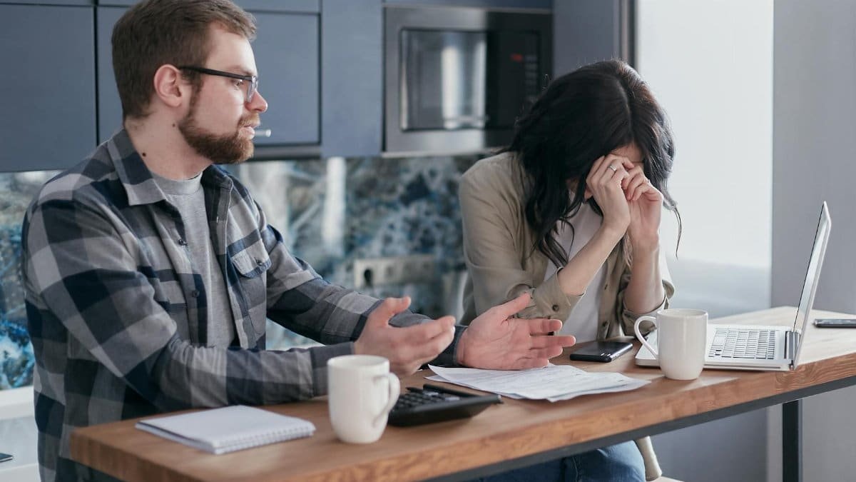 A couple seated at a table, looking stressed while discussing financial issues indoors.