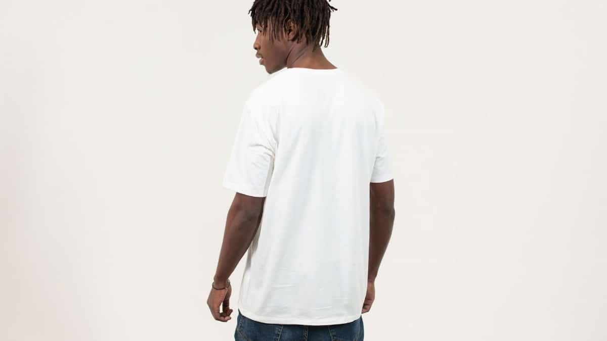 Back view of serious young African American guy with dreadlocks in casual t shirt standing against white background and looking away