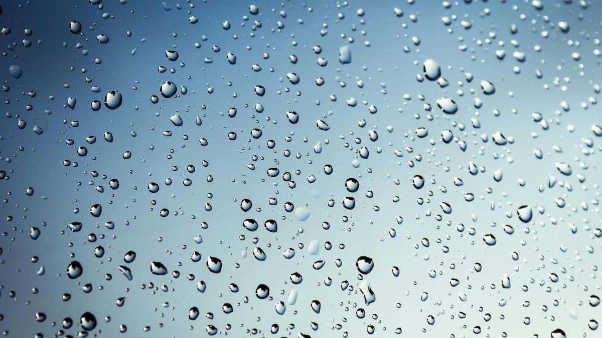 Crystal-clear water droplets on glass against a soft blue backdrop, capturing a rainy day essence.